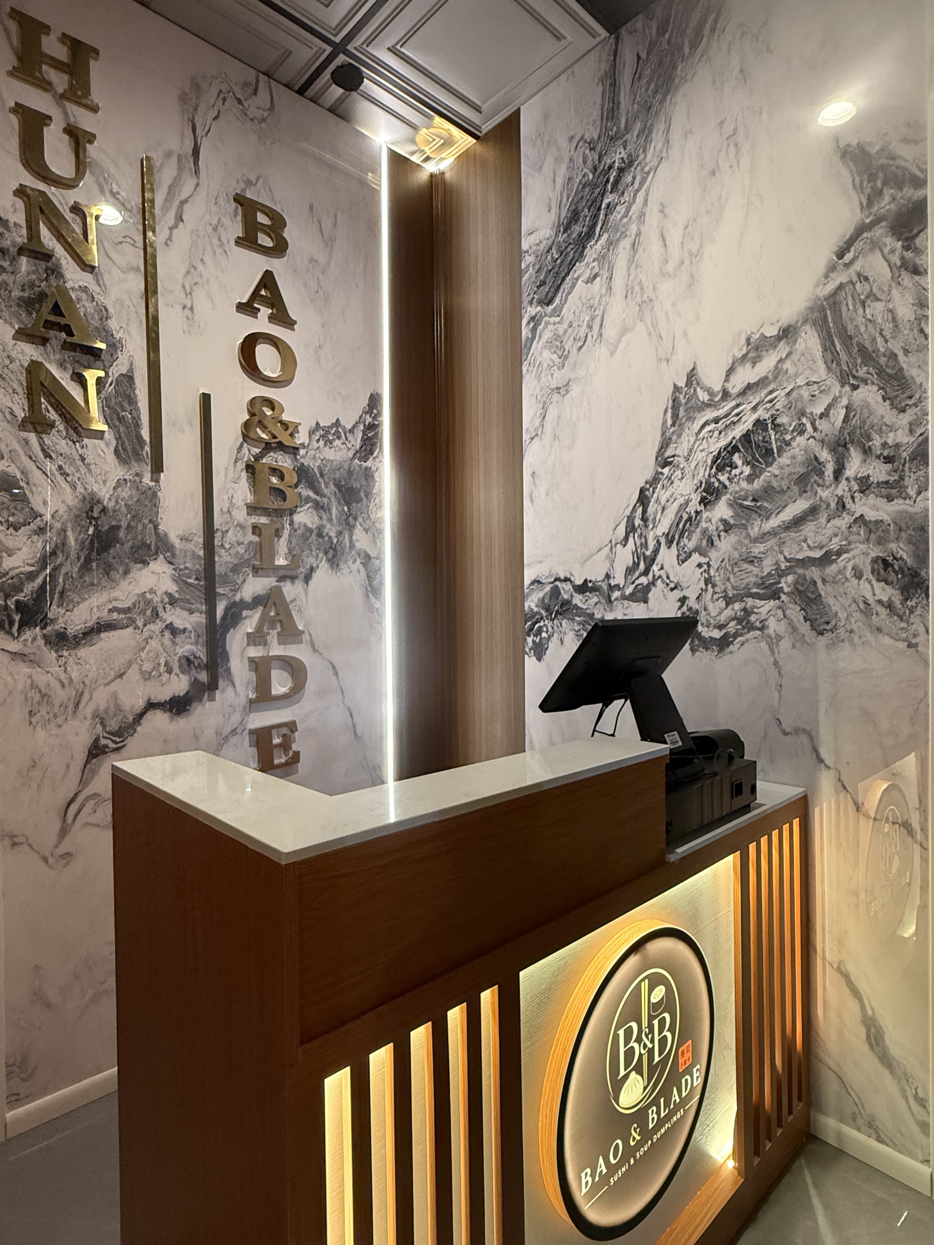 Marble host stand with the gold Bao & Blade signage at the entrance